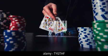 Close up of young man poker player hand holding and showing playing cards betting chips at the casino table. Gambling tournament winner success concep Stock Photo