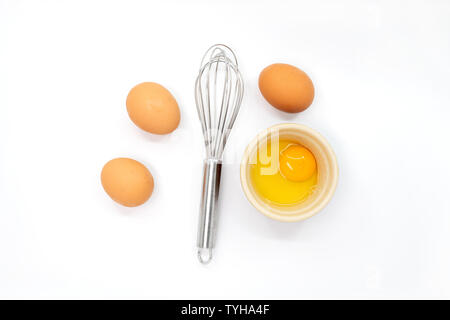 Eggs, a whisk and one egg yolk on a white background Stock Photo
