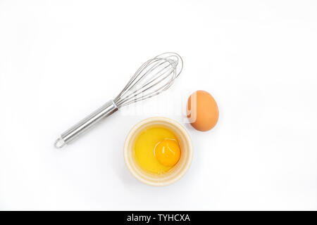 Top view of an egg, egg yolk and whisk on a white background Stock Photo