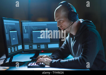 hacker with computer and headset in dark room Stock Photo