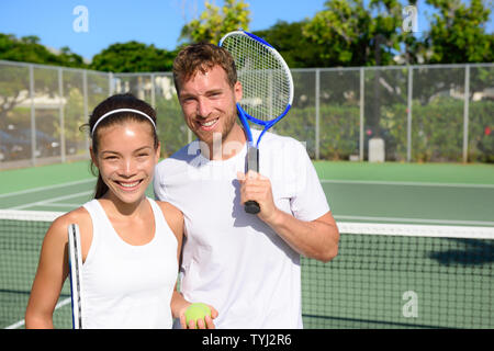 Tennis players portrait on tennis court outdoor. Couple or mixed double tennis partners after playing tennis outside in summer. Happy young people, woman and man living healthy active sport lifestyle. Stock Photo