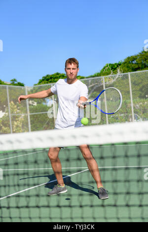 Tennis. Tennis player hitting ball in volley by the net. Male athlete playing outdoors on hard court practicing in summer. Young Caucasian man living healthy active fitness sport lifestyle outside. Stock Photo