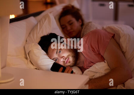 man using smartphone while girlfriend is sleeping Stock Photo