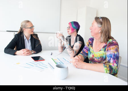 Three women in informal business setting in discussion with paperwork Stock Photo