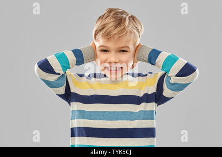 stressed boy in pullover closing ears by hands Stock Photo