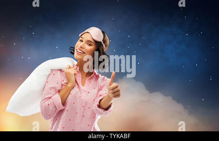 woman with pillow in pajama showing thumbs up Stock Photo