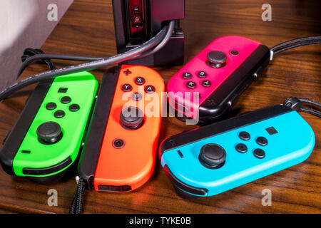 Four Nintendo Switch console game controllers of varying bright colors on a wooden table. Stock Photo