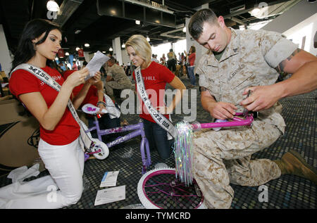 Marine Derrick Smith of Plattsburg, NY, helps out Miss USA contestants Ana Christina Rodriguez, (L) of Texas and Chandra Rae Burnham during the USO Build a Bike event where bikes are assemble and donated to military families at Pier 88 on May 26, 2011 in New York City.    UPI /Monika Graff. Stock Photo