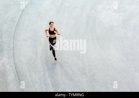 Top view of young attractive athletic woman speed running on city asphalt and workout in the morning time on a sunny summer day. Female runner trainin Stock Photo