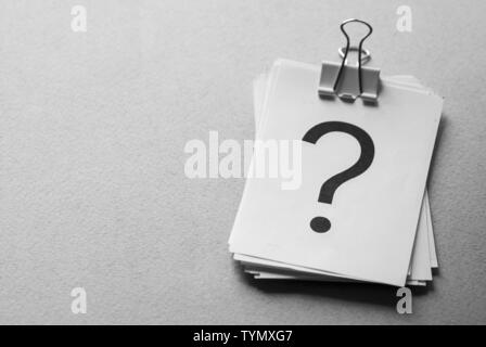 Stack of white cards printed with question marks held together with a metal paper clip over a grey background with copy space Stock Photo