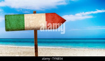 Italy flag on wooden table sign on beach background. There is beach and clear water of sea and blue sky in the background. Stock Photo