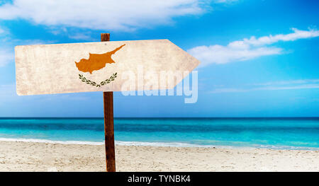 Cyprus flag on wooden table sign on beach background. There is beach and clear water of sea and blue sky in the background. Stock Photo