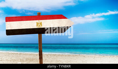 Egypt flag on wooden table sign on beach background. There is beach and clear water of sea and blue sky in the background. Stock Photo