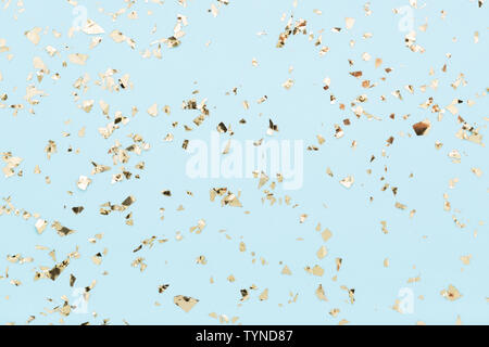 Golden foil confetti on light blue background Festive party or holiday glowing backdrop. Stock Photo