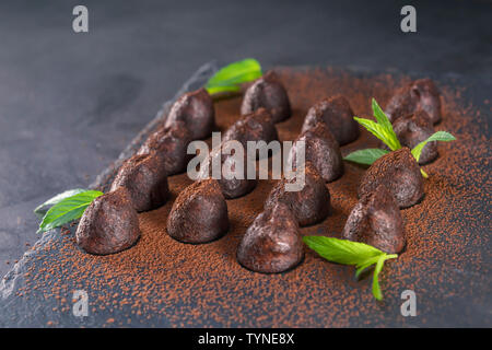 Homemade chocolate truffles with mint sprinkled with cocoa powder on slate. Focus on second truffle in road. Stock Photo