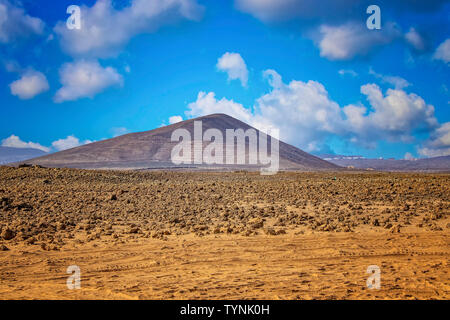 A View of the volcanic hill in the sandy desert. Blue sky with clouds is in the background. It is situated in Fuerteventura, Canary islands, Spain. Stock Photo
