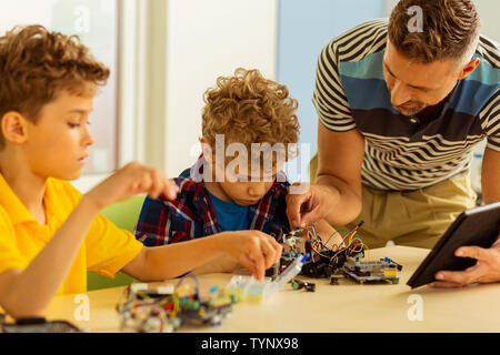 So busy. Nice smart man leaning forward while controlling work of his students Stock Photo