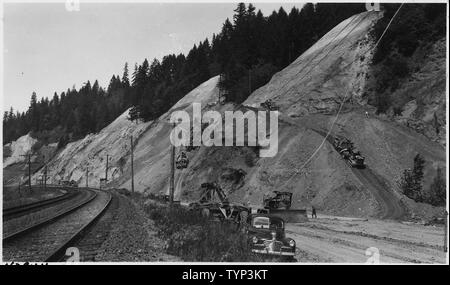 View shows method of excavating high cuts. Cutting at top done by D8 cat. with rooter and bulldozer attachments. Second dozer excavates and assists in loading RD8 cats. with 20' yd. carryall scrapers. Slope is broght down as accruately as possible as work progresses. Cat at left on up road and one at right on down road enroute to fill. Cat. ad dozer in foreground on fill spreading and clean-up of traveled road. Traffic control tower in left background. Roadbed to be 72' wide.; Scope and content:  Pacific Highway, Woodland Stock Photo