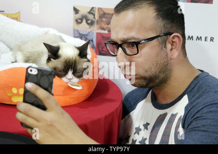 A fan takes a picture with Grumpy Cat when feline internet sensations Grumpy Cat and Oskar the Blind Cat make a special appearance at Bleecker Street Records in New York City on July 16, 2014. The duo will debut their new music video 'Cat Summer' on July 16th. Grumpy Cat will return next month for promotional activities in support of her book, The Grumpy Guide to Life: Observations from Grumpy Cat.    UPI/John Angelillo Stock Photo