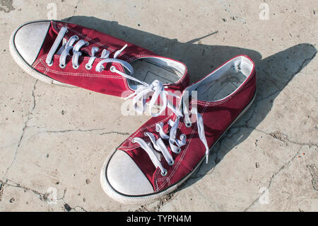 Pair of worn out vintage red old canvas sneakers on outside concrete surface Stock Photo