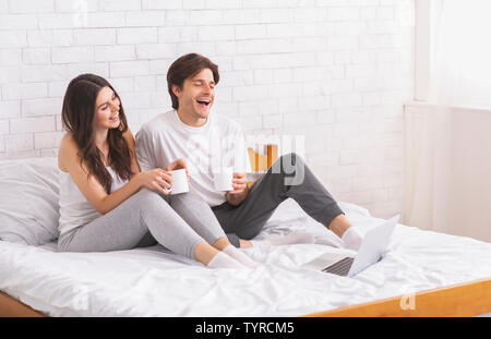 Happy couple enjoying fresh coffee and watching laptop in bed Stock Photo
