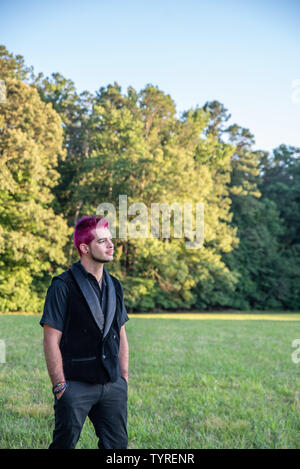 Alternative white caucasian man with pink hair outside gazing in the distance, contemplative. Trees in the background with blank empty room space for Stock Photo