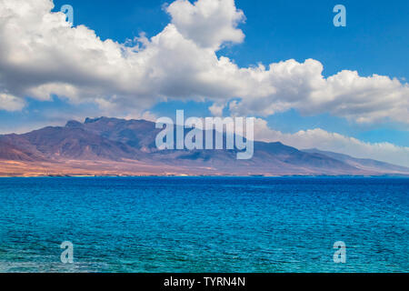 View of the hill on the island Fuerteventura near Morro Jable, Canary islands, Spain. There is clear blue water and beautiful sky. Stock Photo