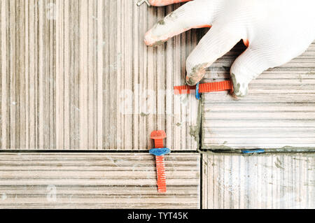 Tiler's hand is using plastic wedges and clips for aligning tiles together. Stock Photo
