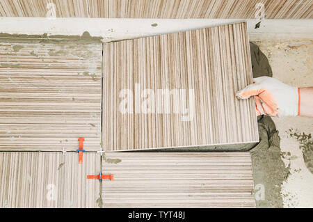 Installation of ceramic tiles. A tile's hand is puting a tile on an adhesive. Top view. Stock Photo