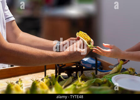 Selling roasted (grilled) corn on street.  Vendor handing grilled corn to customer. Stock Photo