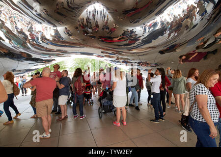 visitors and tourists to millennium park on a  busy saturday morning in summer take photos and selfies underneath the cloud gate bean sculpture in Chi Stock Photo