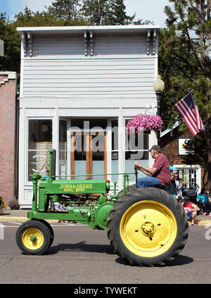 An antique John Deere tractor on parade passes by one of the old stores on main street in Brownsville, Oregon. Stock Photo