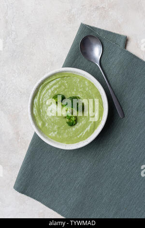 Tasty broccoli cream soup in white bowl on green napkin at bright table. Concept of healthy, fasting food. Above view Stock Photo