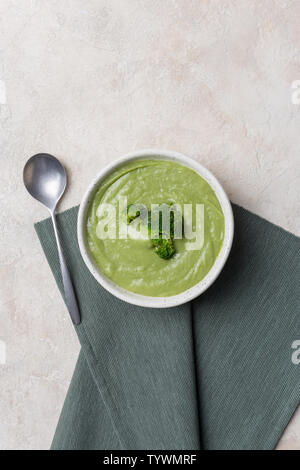 Fresh broccoli cream soup in bowl on light concrete background with napkin and spoon. Concept of spring food. Top view. Stock Photo