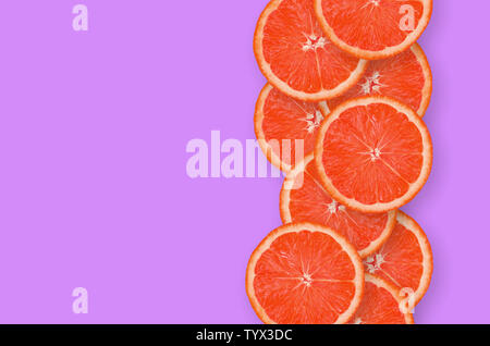 Top view of grapefruit fruit slices on bright purple background. A saturated citrus vertical row with copy space. Minimalistic flat lay Stock Photo