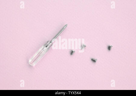 A small screwdriver and a few screws on pink background. Tools for the repair and disassembly of modern smartphones and mobile devices Stock Photo