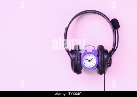 Retro alarm clock with black headphones on pink background. Concept of time to listening music Stock Photo