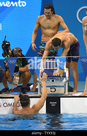 USA's Michael Phelps reaches down to congratulate teammate Nathan Adrian as Cody Miller looks on as they celebrate winning the final of the Men's 4 x 100m Medley Relay at the Olympic Aquatics Stadium at the 2016 Rio Summer Olympics in Rio de Janeiro, Brazil, on August 13, 2016.  The United States won the gold medal setting a new Olympic Record with a time of 3:27.95.         Photo by Richard Ellis/UPI.. Stock Photo