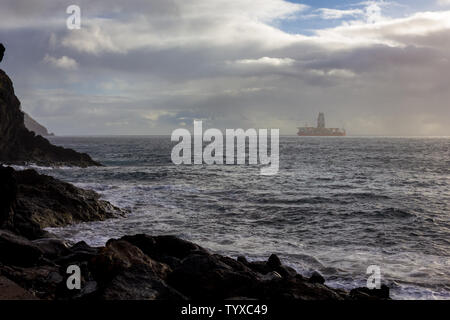View of an offshore oil drilling platform standing near the coast under the rain on a cloudy day Stock Photo