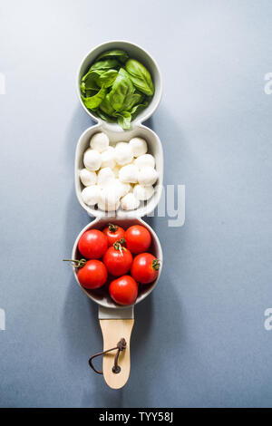 Tomato basil and mozzarella. Food Ingredients pattern with mozarella cheese balls and fresh basil leaves, round cherry tomatoes, top view on a pink ba Stock Photo