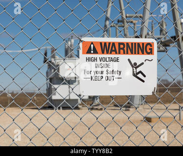 High voltage warning sign showing danger of electrocution on a chain link fence surrounding an electrical substation supplying electricity Stock Photo