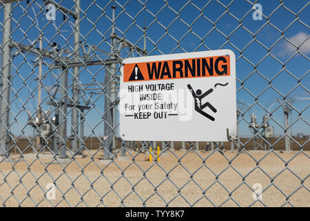 High voltage warning sign showing danger of electrocution on a chain link fence surrounding an electrical substation supplying electricity Stock Photo