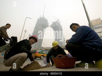 Chinese migrant laborers mix concrete on a new sidewalk running through Beijing's Central Business District and past the futuristic CCTV Tower under construction on November 10, 2007.  CCTV's new 550,000 square meter headquarters, to be completed for the Beijing Olympics in 2008, will be among the first of 300 towers to be constructed in Beijing's new Central Business District. (UPI Photo/Stephen Shaver) Stock Photo