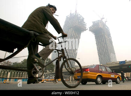 A Chinese migrant laborer cycles past the futuristic CCTV Tower under construction on November 10, 2007.  CCTV's new 550,000 square meter headquarters, to be completed for the Beijing Olympics in 2008, will be among the first of 300 towers to be constructed in Beijing's new Central Business District. (UPI Photo/Stephen Shaver) Stock Photo
