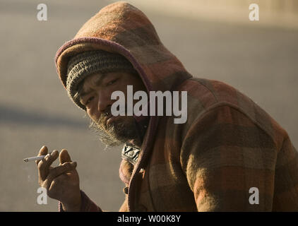 A Chinese homeless man smokes a cigarette on the sidewalk in downtown Beijing January 16, 2009. The politically divisive income gap between China's affluent citydwellers and its huge rural population expanded to its widest level ever last year as the economy slowed, putting millions of rural migrants out of work.  (UPI Photo/Stephen Shaver) Stock Photo