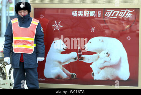 A Chinese traffic warden stands next to a Coca-Cola advertisement celebrating Christmas and the holidays on a street in Beijing on December 17, 2014.  Christmas has become China's number one imported holiday, followed by Valentine's Day and Halloween.  Cities across China are blinking with fairy lights, fancy hotels are flaunting trees with tinsel and decorations and glossy Chinese magazine covers display holiday recipes and table settings.       UPI/Stephen Shaver Stock Photo