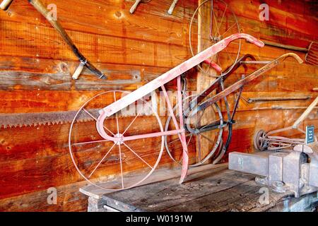 An antique plow sits on a table in a barn surrounded by other old farm tools Stock Photo
