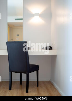 Makeup corner, black chair, black hair dryer in front of the mirror and lamp on the wall in hotel room vertical style. Stock Photo