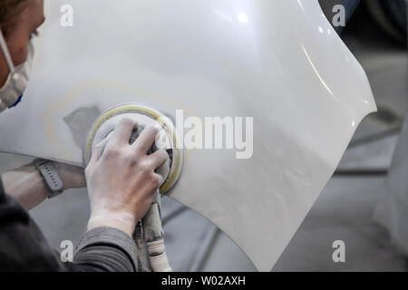 Preparation for painting a car element using sander and putty by a service technician leveling out before applying a primer after damage to a part of Stock Photo