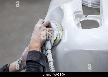 Preparation for painting a car element using sander and putty by a service technician leveling out before applying a primer after damage to a part of Stock Photo